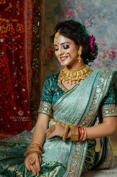 a woman in a green and gold sari sitting on the ground with her hands clasped to her chest