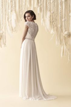 a woman in a long white dress standing next to a wall with feathers hanging from it