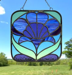 a stained glass window hanging from a chain in front of a green field and blue sky