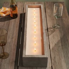 candles are lit in a rectangular box on a table next to two wine glasses and a bottle