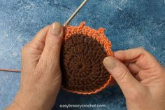 someone is crocheting an orange piece of yarn on the ground with their hands