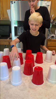 a young boy standing in front of red and white cups on top of a table