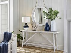 a white table topped with a mirror next to a blue chair and vase filled with flowers