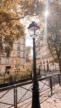 a lamp post in the middle of a park with trees and buildings on either side