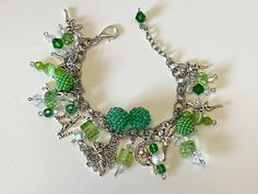 a close up of a bracelet with charms on a white surface and a green bead