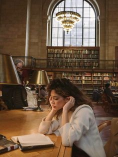 a woman sitting at a table with a book in front of her, reading and talking on the phone