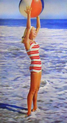 a woman in striped bathing suit holding an orange and white frisbee over her head