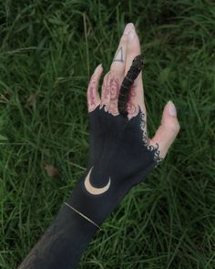 a person's hand with tattoos holding up a black and white glove that has a snake on it