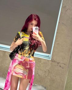 a woman with red hair taking a selfie in front of a window while wearing a colorful dress