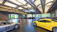 several sports cars are parked in a large room with high ceilings and glass doors on the windows