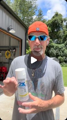 a man in an orange hat and sunglasses holds up a bottle of deodorant