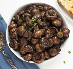 a white bowl filled with mushrooms next to a slice of bread on top of a blue napkin