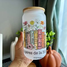 a person holding up a jar that has books on it and flowers in the background