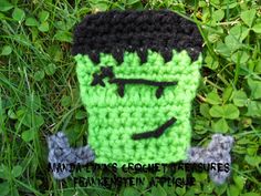 a green and black crocheted bag with a face on it sitting in the grass