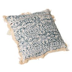 a blue and white pillow with tassels on the edges, sitting on a white surface