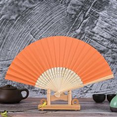 an orange fan sitting on top of a wooden table next to teapots and cups