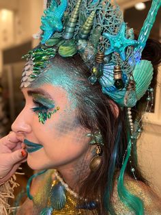 a woman with blue and green makeup is wearing an elaborate headdress while holding her finger to her mouth