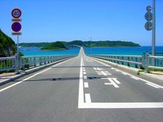 an empty road with no cars on it next to the ocean and blue water in the background