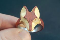 a person holding a wooden ring with a fox head on it's side and the other hand