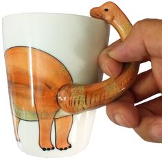 a hand holding a coffee cup with an animal painted on the side and various mugs around it