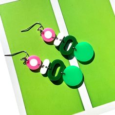 three pairs of earrings are sitting on a green surface with white and pink circles hanging from them