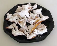 a black plate filled with powdered sugar covered pastries on top of a white table