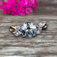 an engagement ring with three stone accents on top of a wooden table next to pink flowers