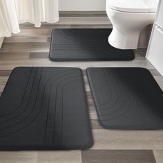 two black bath mats sitting on top of a bathroom floor next to a white toilet