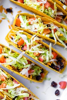 several tacos are lined up on a white plate with black olives and lettuce