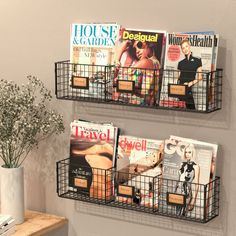 two wire baskets holding magazines and magazines on the wall next to a vase with flowers