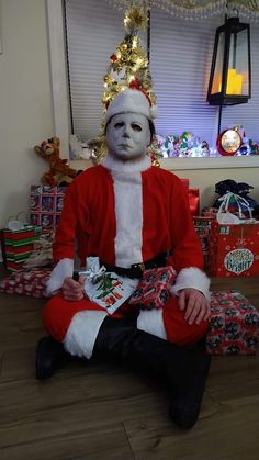 a man dressed as santa claus sitting in front of a christmas tree