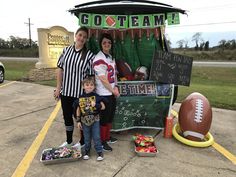 two women and a child are standing in front of a football stand that is decorated for the game