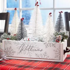 christmas trees in a wooden box on a plaid tablecloth with red and white decorations