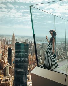 a woman standing on top of a tall building in a dress and hat looking at the city