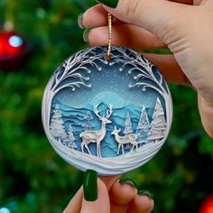 a hand holding up a christmas ornament with two deers in the woods