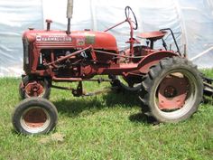 an old red tractor sitting on top of a grass covered field in front of a white tarp