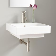 a white sink sitting under a mirror next to a wall mounted faucet with a single pink flower in it