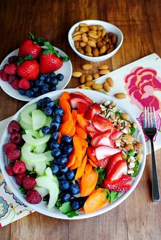 two white plates filled with fruit and nuts on top of a wooden table next to silverware