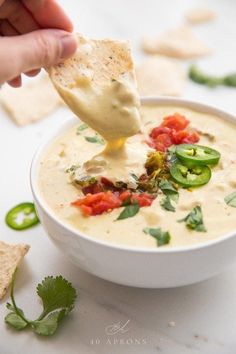 a person dipping tortilla chips into a bowl of quesadilla soup