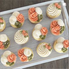 cupcakes with white frosting and orange flowers are arranged in rows on a tray