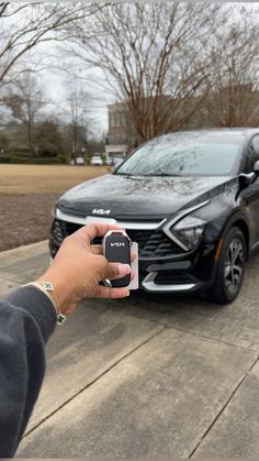 a person holding a cell phone in front of a black car on the side of the road