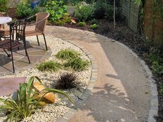 a patio area with chairs and table surrounded by rocks, gravel and plants in the foreground