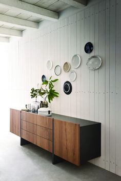 a wooden sideboard with plates on the wall and a plant sitting on top of it