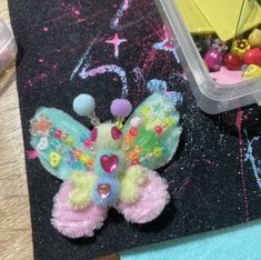 there is a small colorful butterfly on the table next to some beads and other things