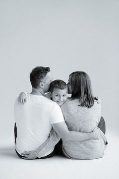 a black and white photo of a family sitting on the floor with their arms around each other