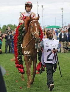 the jockey is walking his horse down the field with flowers on it's back