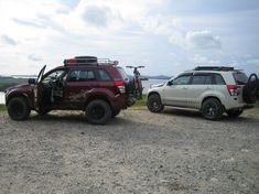 two vehicles parked on the side of a dirt road next to a body of water