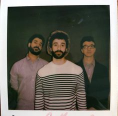 three men standing next to each other in front of a black and white photo with pink writing on it