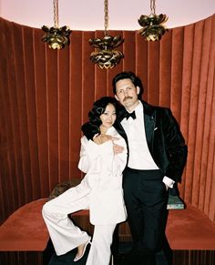 a man and woman pose for a photo in front of a red velvet wall with chandeliers