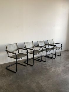 four chairs sitting next to each other in a white walled room with concrete flooring